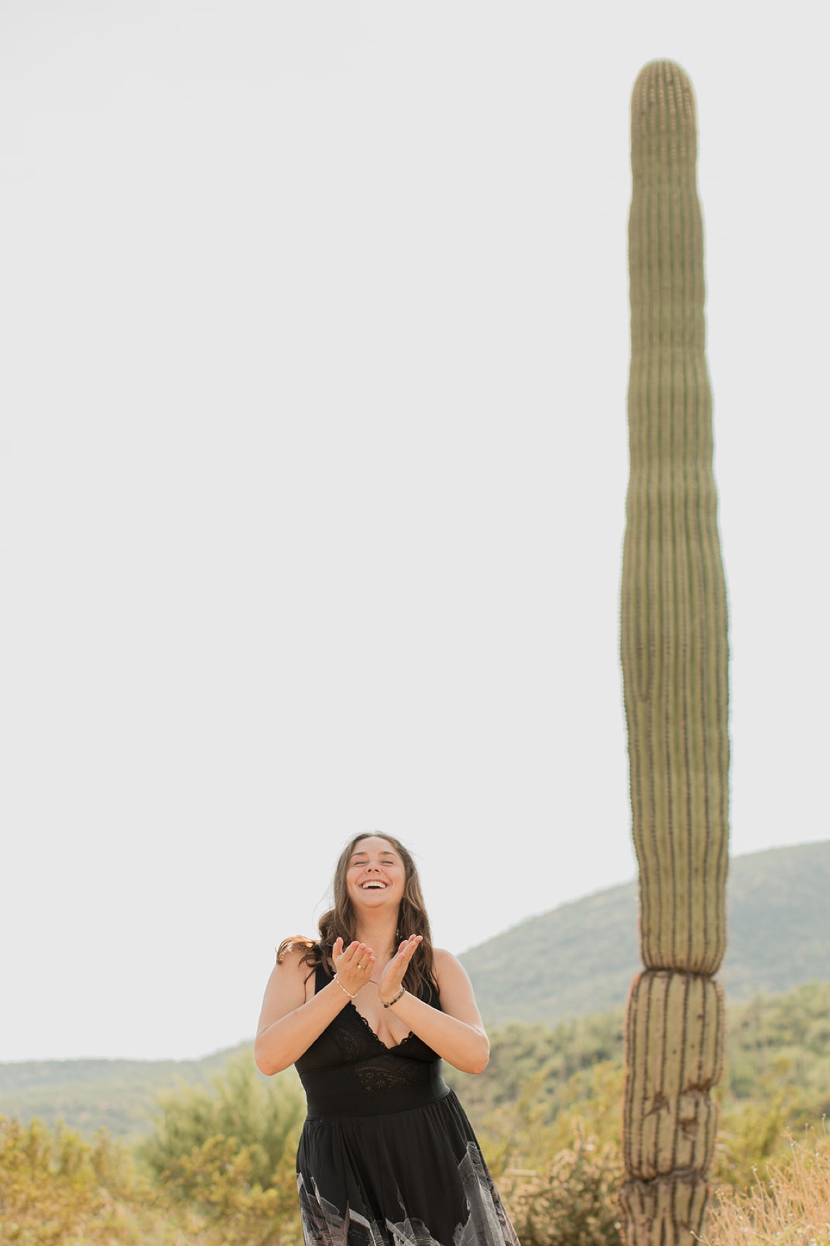 Heather Flynn in the desert with hands at her heart, eyes closed and smiling joyfully beside a saguaro cactus